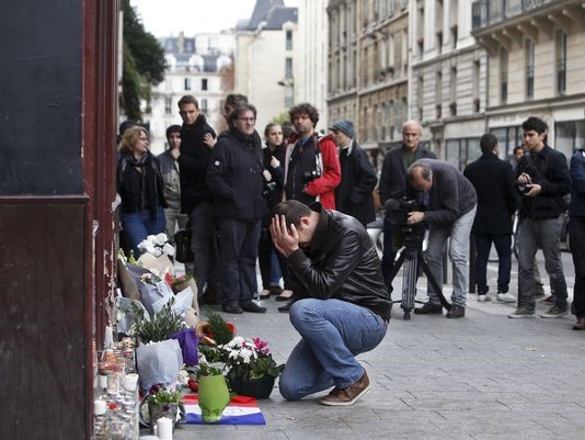 A man holds his head in his hands while placing flowers a memorial in Paris. 
